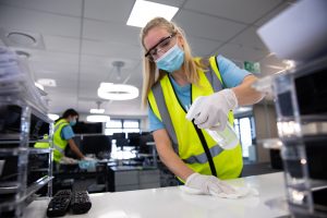 woman wearing hi vis vest and face mask cleaning the office using disinfectant